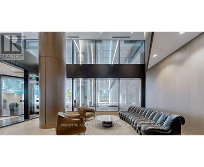 A modern waiting area with a long black leather couch and a wooden floor.