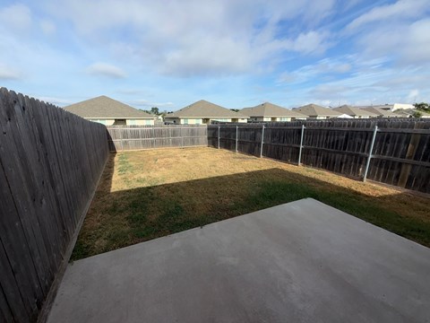 A backyard with a concrete slab and a wooden fence.