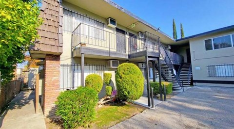 A two-story apartment building with a balcony and a small garden in front.