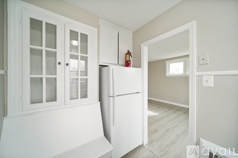A white refrigerator is in a kitchen with a white cabinet and a white bench.
