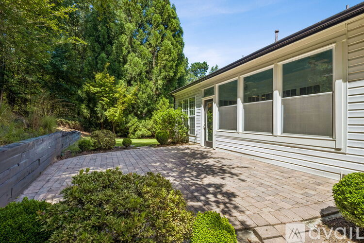 A house with a grey siding exterior and a brick patio surrounded by greenery.