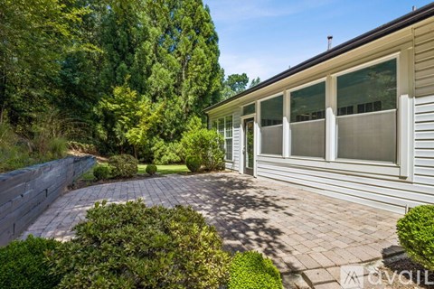 A house with a grey siding exterior and a brick patio surrounded by greenery.