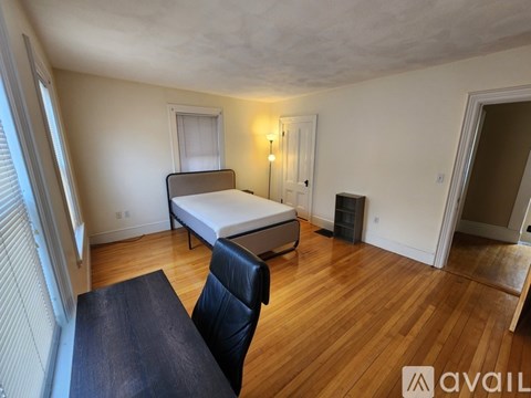 A bedroom with a bed, chair, and wooden floors.