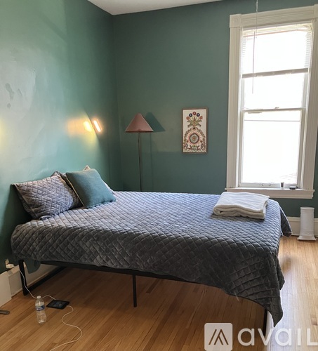 A bed with a grey comforter and a white pillow is in a room with green walls.