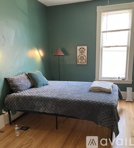A bed with a grey comforter and a white pillow is in a room with green walls.