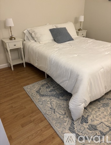A bedroom with a white bed and a grey patterned rug.