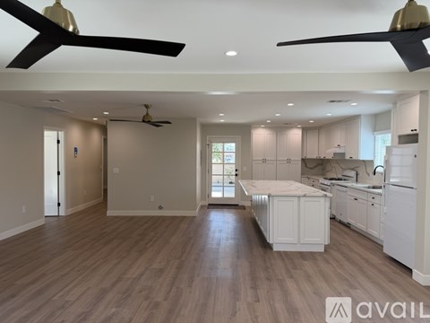A spacious kitchen and living room with hardwood floors and ceiling fans.