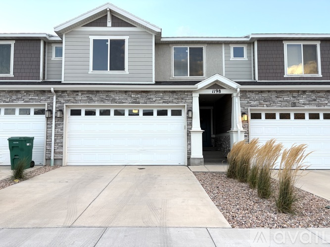 A grey house with a white garage door and a green trash bin.