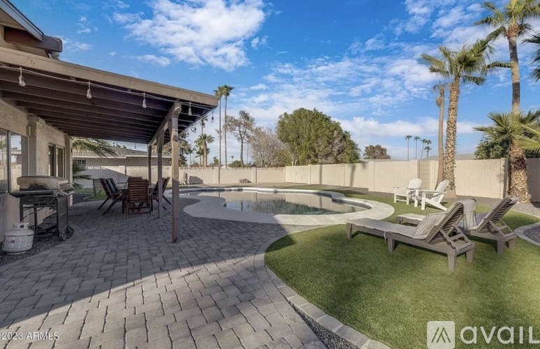 A backyard with a patio, a pool, and a lawn.