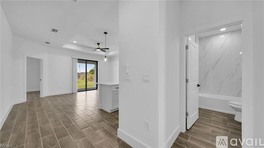 A spacious room with a ceiling fan and a sliding glass door leading to a balcony.