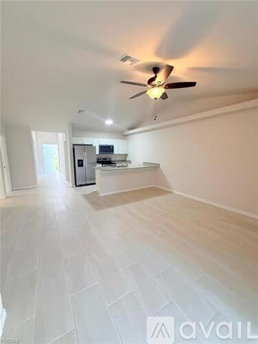 A spacious room with a ceiling fan and a kitchen area in the background.