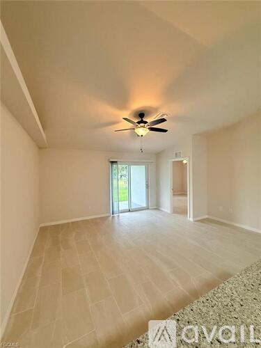 A spacious room with a ceiling fan and light, tiled flooring, and a door leading to a balcony.