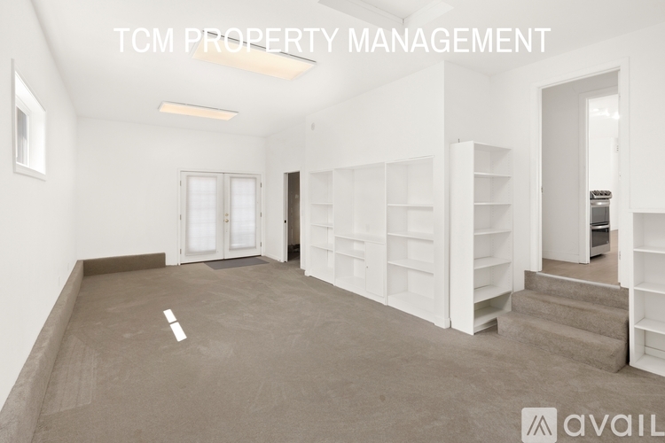 A spacious room with white shelves and a staircase leading to another room.