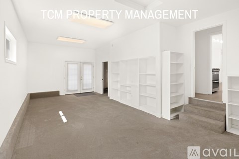 A spacious room with white shelves and a staircase leading to another room.