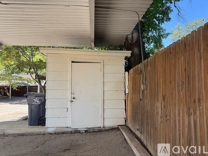 A small white building with a door and a trash can outside.