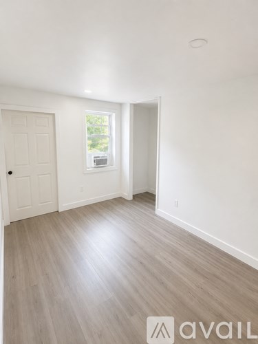 A room with a white door and a window with a view of trees.