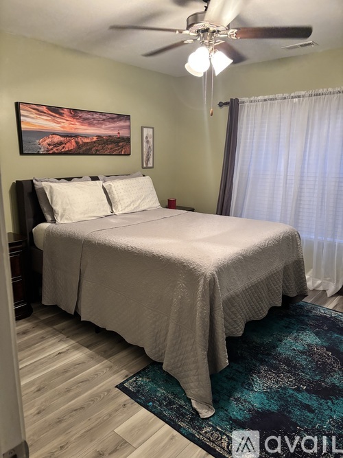 A bedroom with a bed, a ceiling fan, and a painting on the wall.