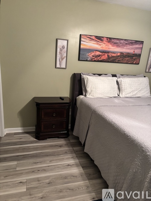 A bedroom with a bed, nightstand, and a painting on the wall.