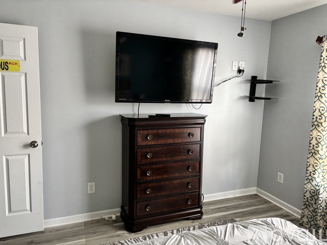 A bedroom with a dresser and a flat screen TV mounted on the wall.