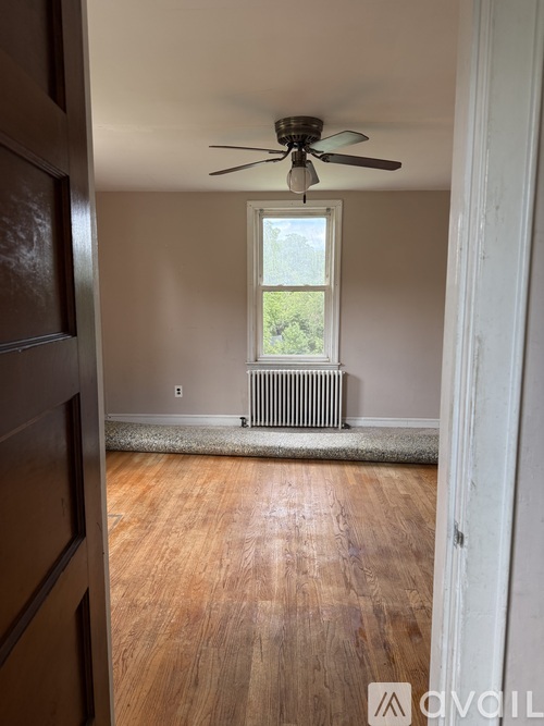 A room with a ceiling fan and a window with a view of trees.