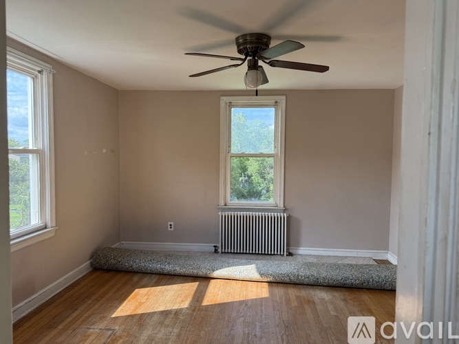 A room with a ceiling fan, a window with a view of trees, and a radiator under the window.
