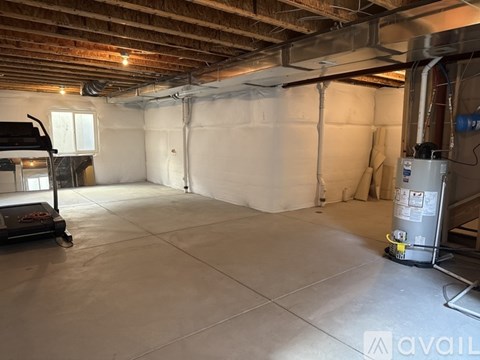 A spacious basement with a concrete floor and white walls, equipped with a water heater and a window.