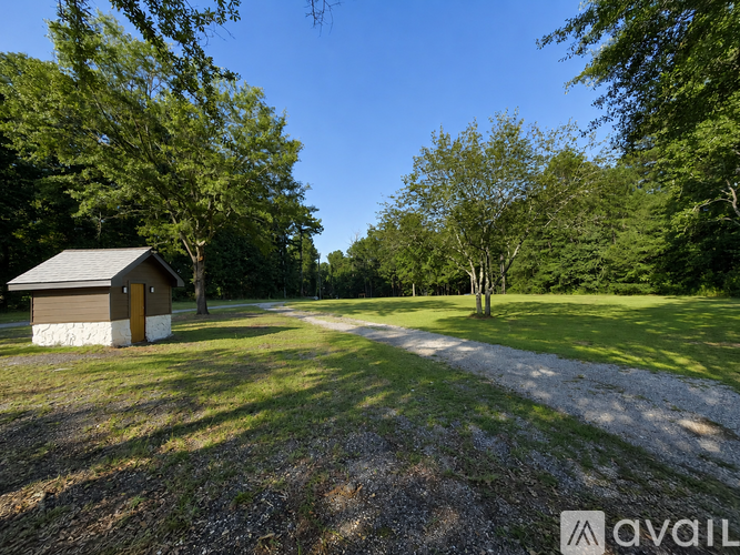 A small building sits in a grassy field with trees in the background.