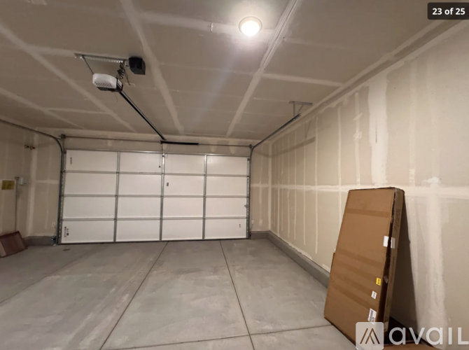 A cardboard box is leaning against a wall in a spacious, empty room with a white garage door in the background.