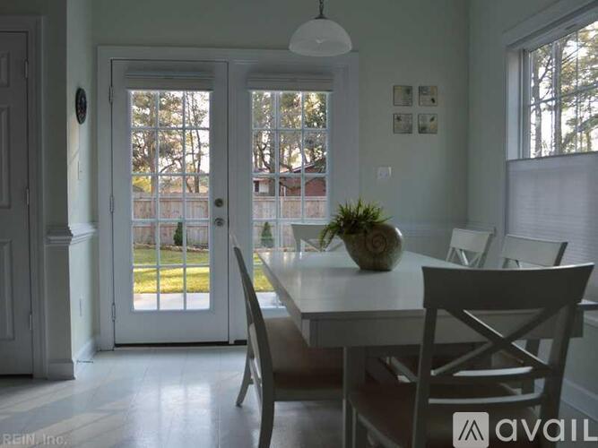 A dining room with a table and chairs and a view of a backyard through the door.