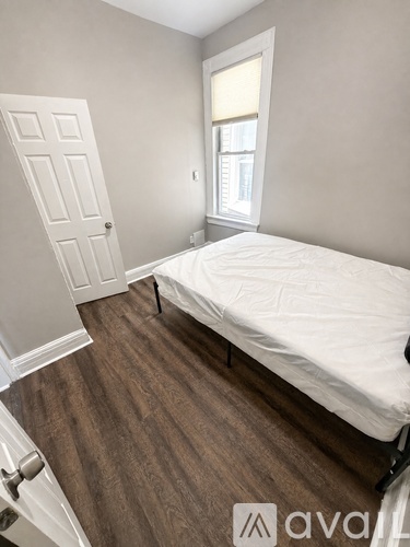 A bedroom with a bed, wooden floor, and a window with blinds.