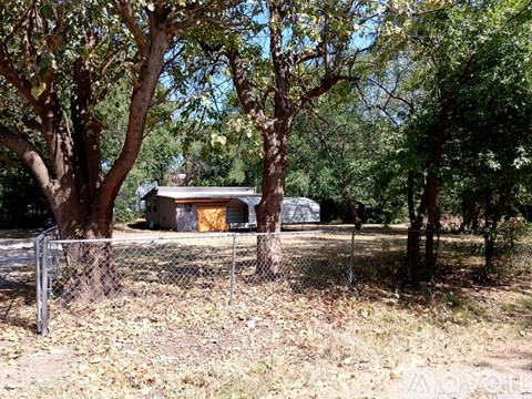 A small building is surrounded by trees and a fence.