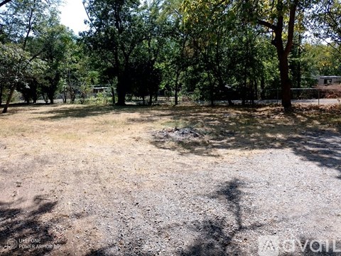 A gravel area surrounded by trees with a fence in the background.