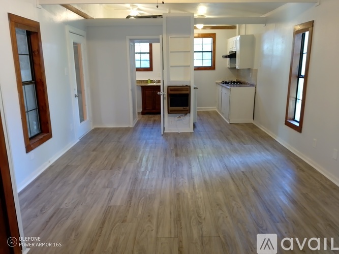 A spacious room with wooden flooring and a kitchen area in the background.