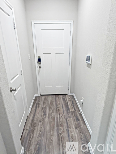 A white door with a black handle is in the middle of a hallway with wood flooring.