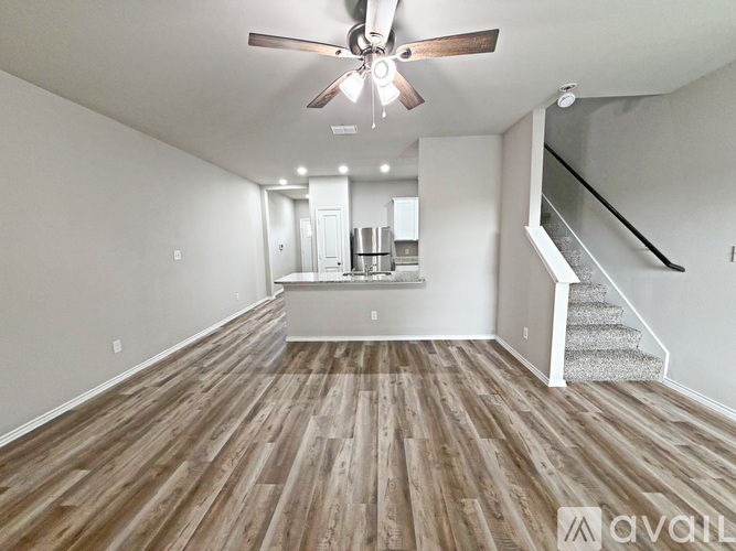 A spacious room with wooden flooring and a staircase on the right side.