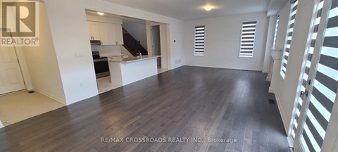 A spacious room with wooden flooring and white walls, with a logo that reads "REALTOR" in the top left corner.