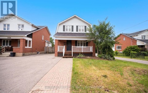 A house with a brick driveway and a white house with a porch in the background.