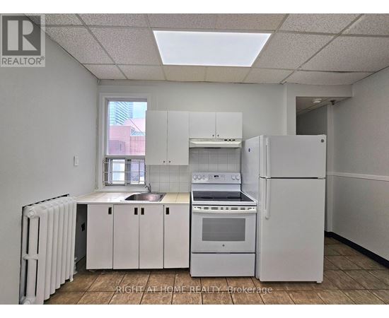 A white kitchen with a refrigerator, sink, and stove.