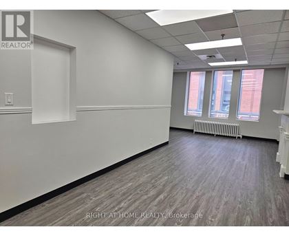 A room with a white wall and a window with a view of a red building.