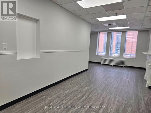 A room with a white wall and a window with a view of a red building.