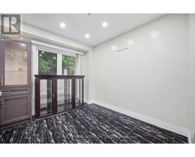 A room with a black and white floor, a window with a view of trees, and a cabinet with glass doors.