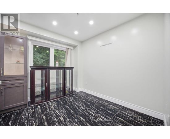 A room with a black and white floor, a window with a view of trees, and a cabinet with glass doors.