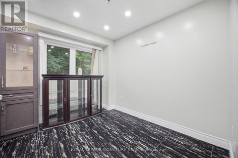 A room with a black and white floor, a window with a view of trees, and a cabinet with glass doors.