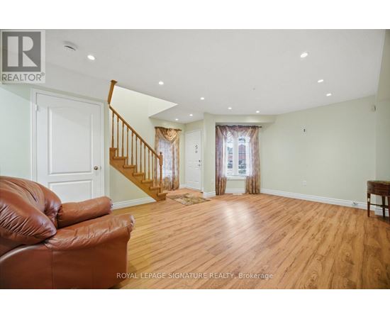 A brown leather couch sits in a spacious living room with wood floors and white walls.