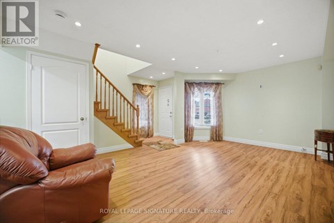 A brown leather couch sits in a spacious living room with wood floors and white walls.