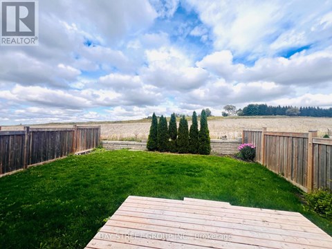 A wooden deck overlooks a grassy backyard with a fence and trees.