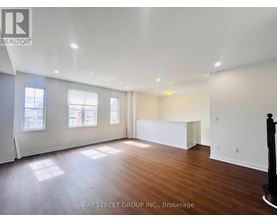 A spacious room with wooden floors and white walls, with a large window on the left side.