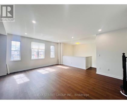 A spacious room with wooden floors and white walls, with a large window on the left side.