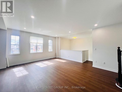 A spacious room with wooden floors and white walls, with a large window on the left side.
