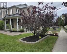 A tree with red leaves is in front of a grey house.